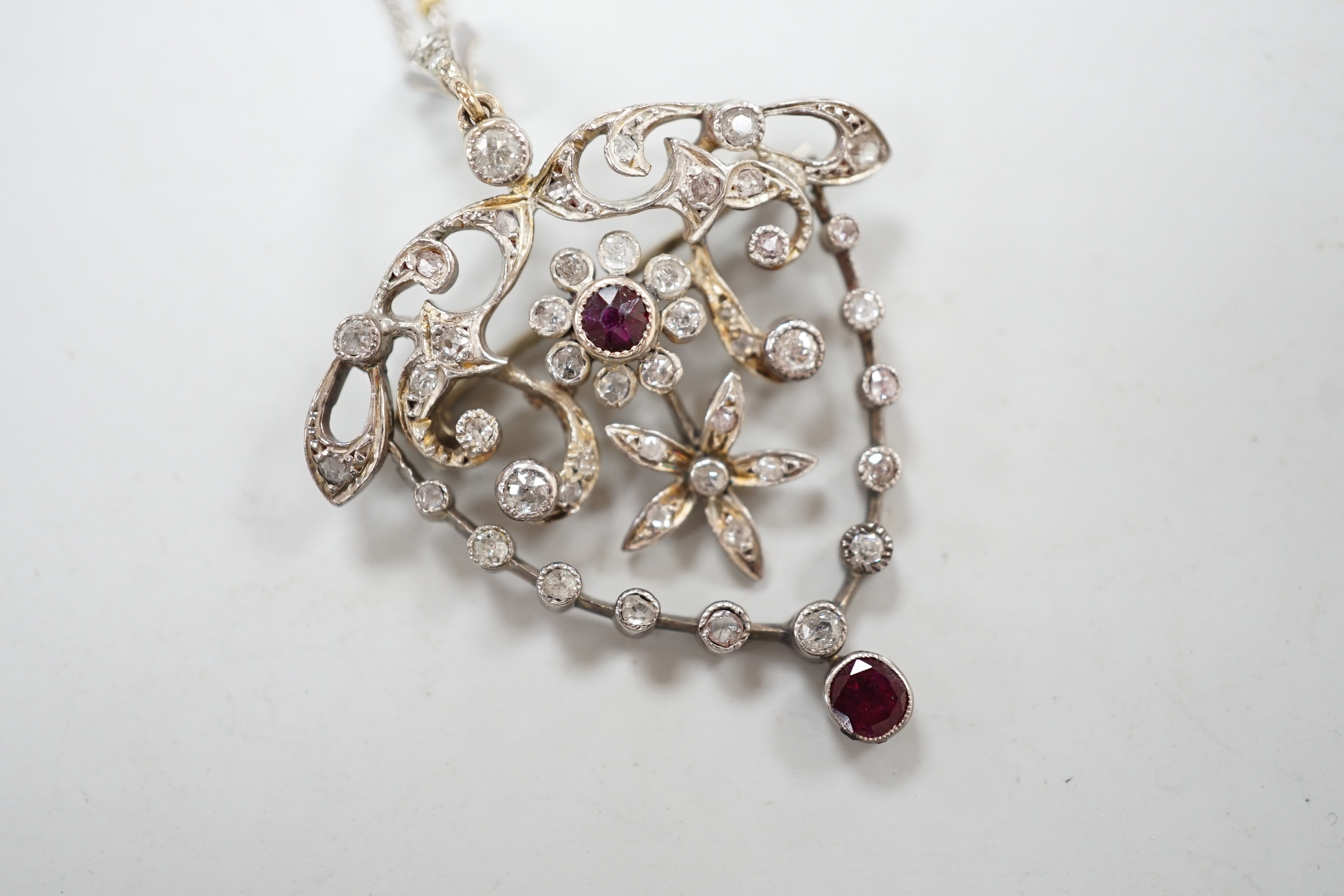 A yellow and white metal, ruby and diamond cluster set drop pendant brooch, 49mm, on an 18ct gold chain, 42cm, gross weight 11.5 grams.
